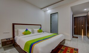 A hotel room with a large bed, a wooden headboard, a nightstand, a bedside table, a wardrobe, and a mirror. - Treebo Down Town, Dalhousie (Dalhousie)