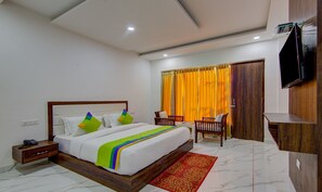 A hotel room with a large bed, a wooden nightstand, a desk with a chair, a TV mounted on the wall, and a window with curtains. - Treebo Down Town, Dalhousie (Dalhousie)
