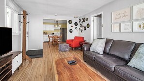 Un salon moderne avec un plancher en bois, un canapé en cuir, un fauteuil rouge et, au fond, un coin repas.