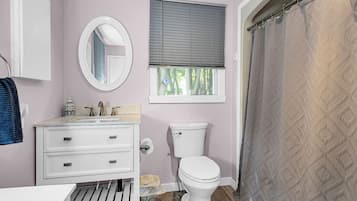 Une salle de bain équipée de toilettes, d’un lavabo, d’un miroir et d’une fenêtre avec des stores.