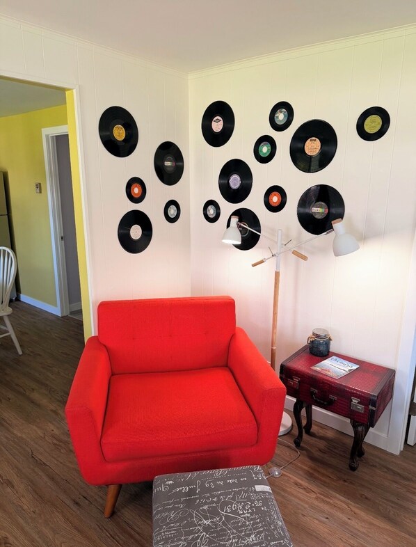 Una habitación con un sillón rojo, una lámpara de pie y un muro decorado con discos de vinilo.