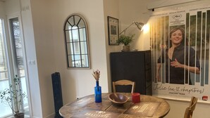 Un comedor con una mesa redonda de madera, sillas, un florero azul, una vela roja y un cartel en la pared.