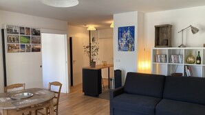 Una sala de estar con un sofá azul oscuro, una mesa de comedor de madera y una planta en maceta.