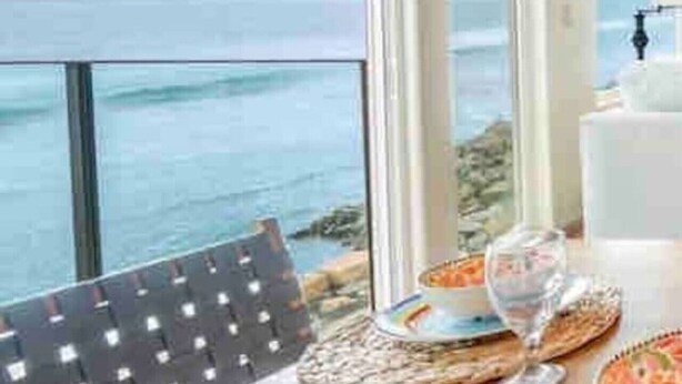 Un coin repas avec vue sur l’océan, une table dressée avec des assiettes et des verres, et une chaise.