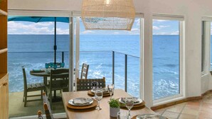 Un coin repas avec une table dressée pour deux personnes, donnant sur l’océan grâce à de grandes fenêtres.