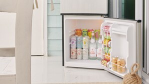 Une cuisine avec un réfrigérateur blanc, un luminaire suspendu et une variété de bouteilles et de boîtes de conserve colorées sur l’étagère de la porte.