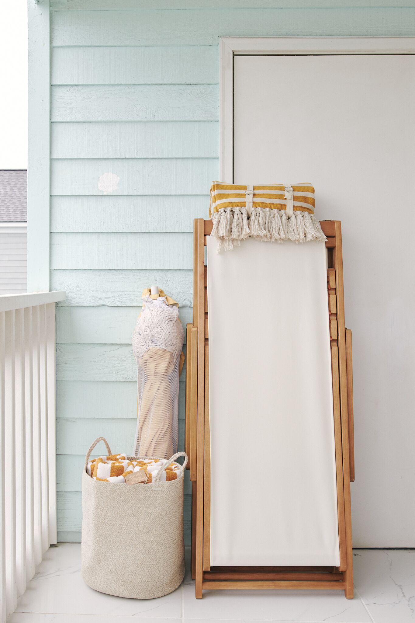 Un chevalet en bois avec une toile blanche, un panier de rangement beige contenant une couverture jaune et blanche, et une porte blanche sur un mur bleu clair.