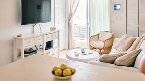Un salon moderne avec un téléviseur à écran plat, un canapé blanc, un fauteuil en osier et une table basse ronde.