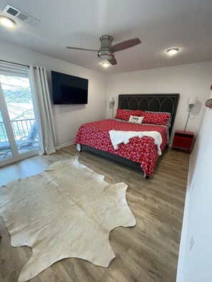 A bedroom with a bed, a ceiling fan, a mounted TV, and a sliding glass door to the outside.