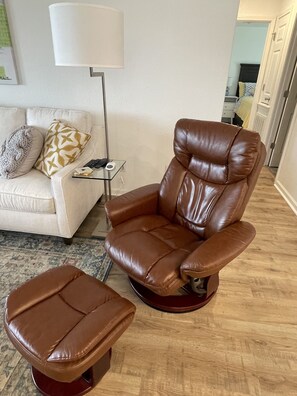 A brown leather recliner with a footrest and a glass coffee table with a remote control.