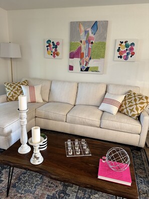 A living room with a beige sofa, patterned cushions, a wooden coffee table, and abstract art on the walls.