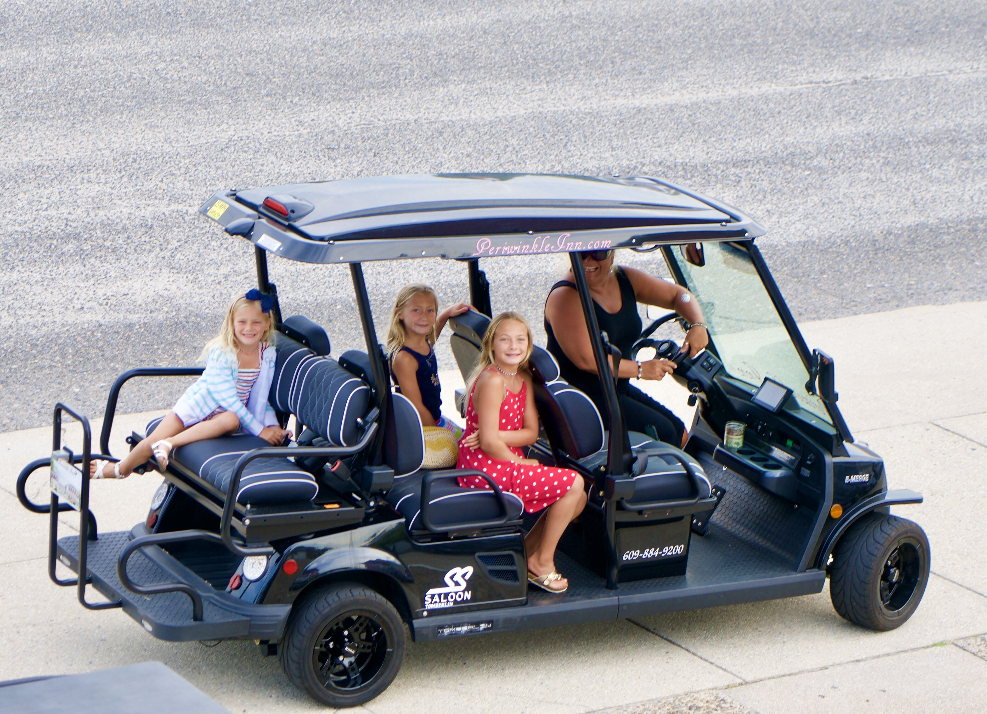 Un golf cart con tre passeggeri, tra cui un guidatore, su una superficie pavimentata.