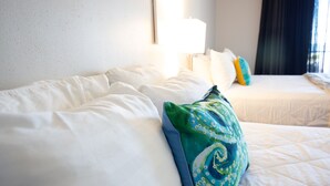 Habitación de hotel con dos camas, ropa de cama blanca y un cojín estampado en verde.