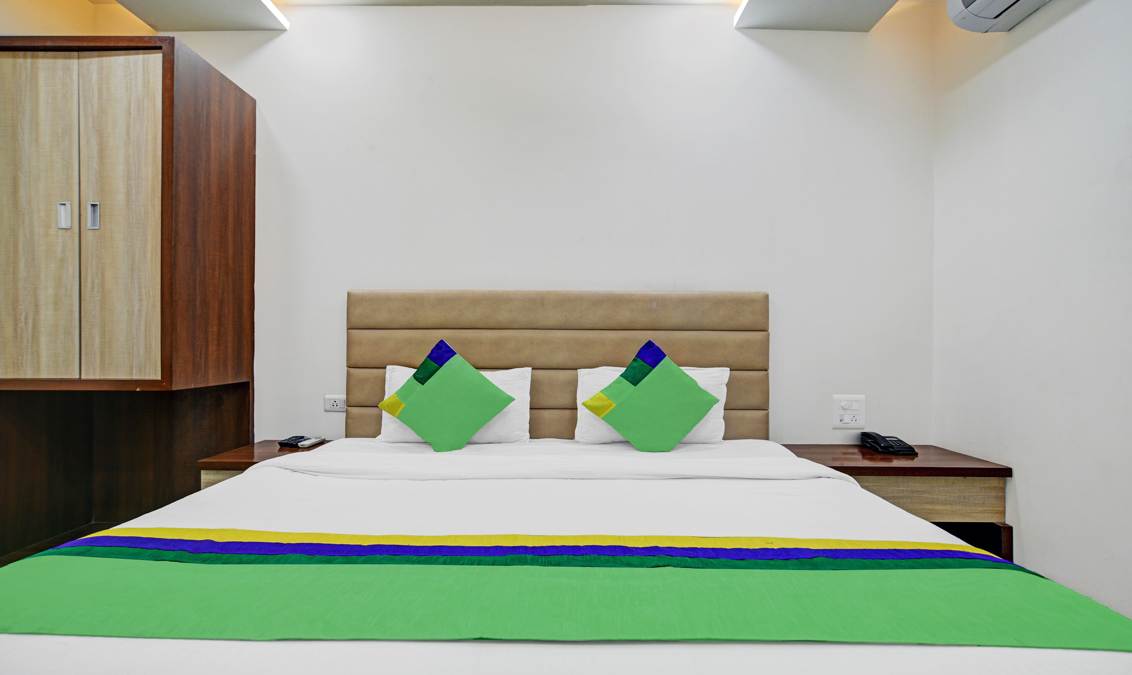A hotel room with a bed, a wooden wardrobe, and a nightstand with a phone.