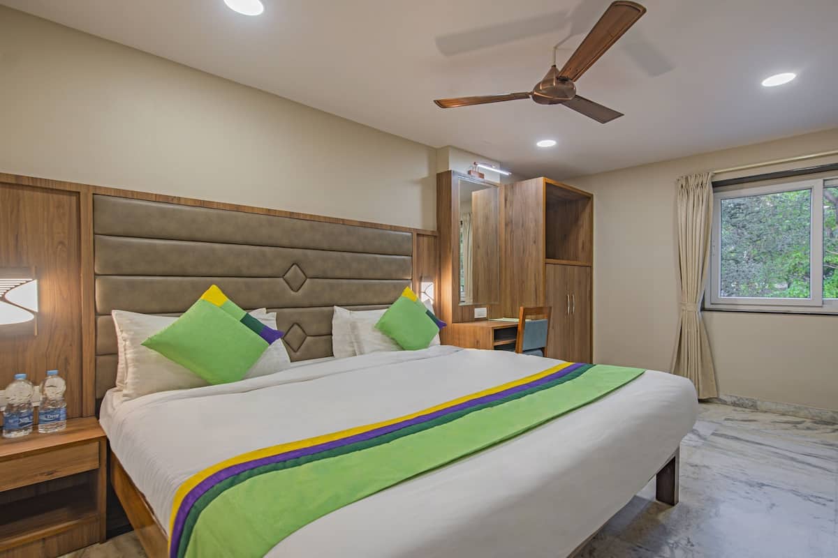 Quarto de hotel com cama, ventilador de teto, janela com vista e armário de madeira.