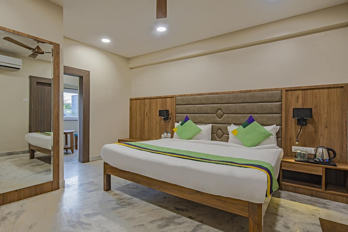 Quarto de hotel com cama grande, cabeceira de madeira, mesas de cabeceira, espelho e ventilador de teto.