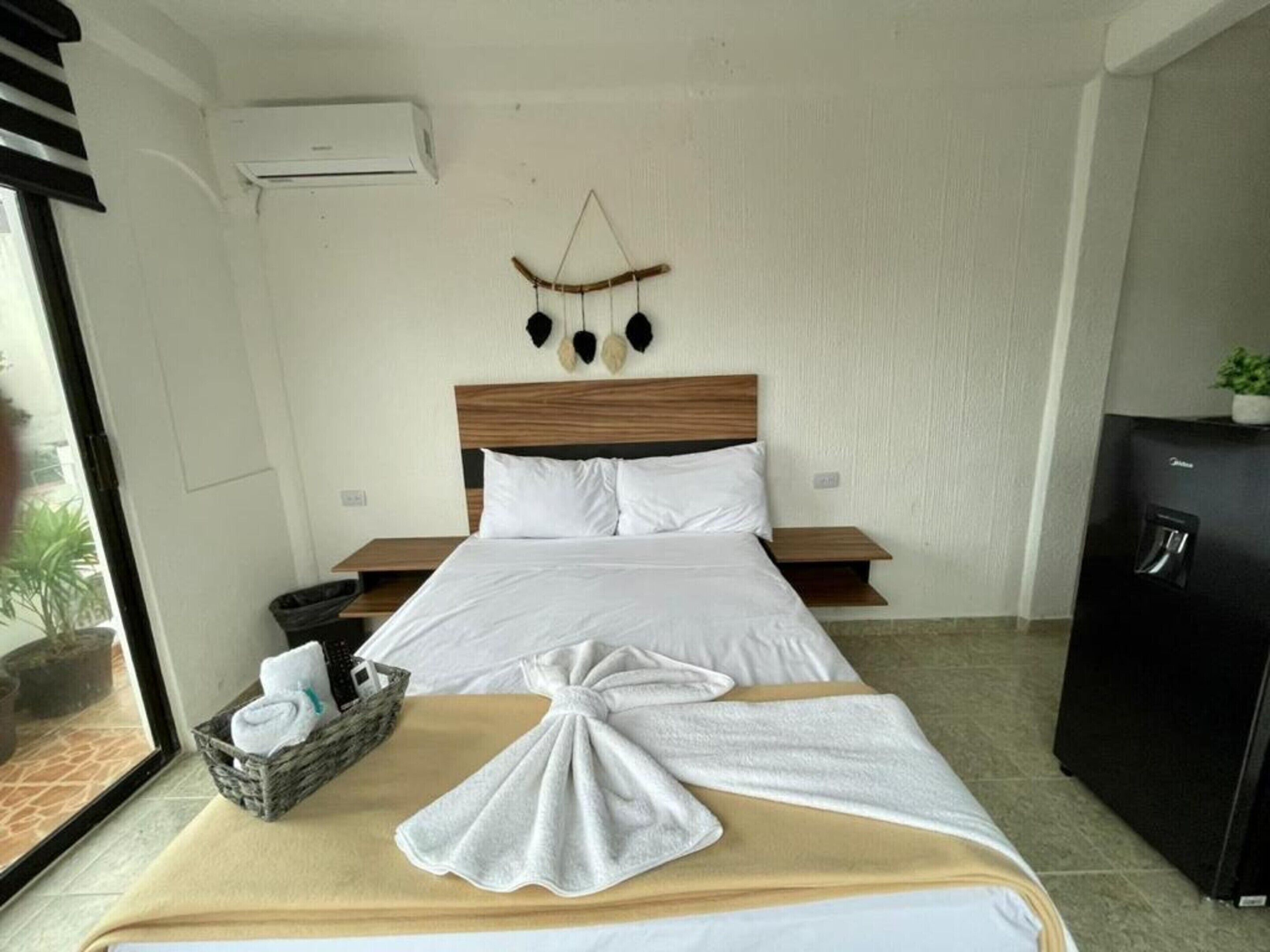 A hotel room with a bed, a bedside table, a small cabinet, and a wall-mounted air conditioner.