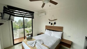 A bedroom with a bed, a ceiling fan, a TV mounted on the wall, and a view of the outdoors through a sliding door. - MAYAB Playa - 5Th. Ave (Playa del Carmen)