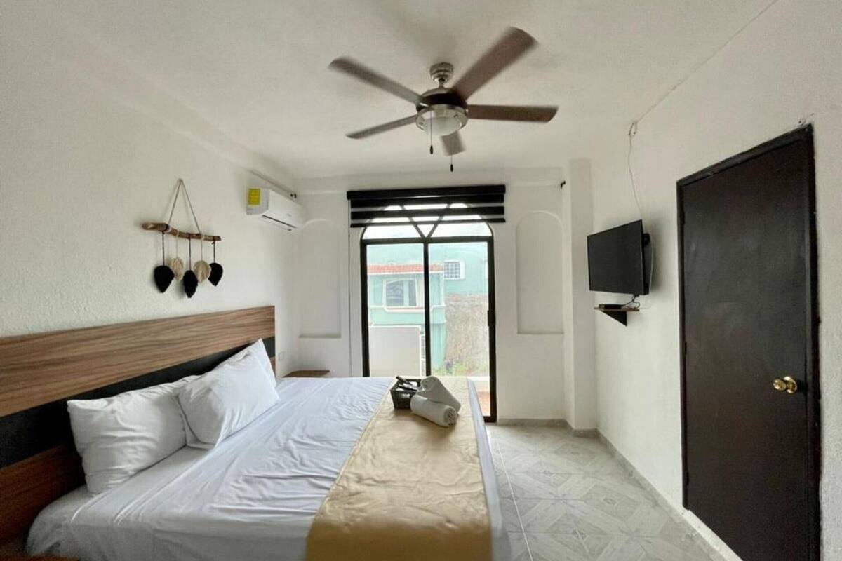 A hotel room with a bed, a ceiling fan, a TV, and a view of the outside.