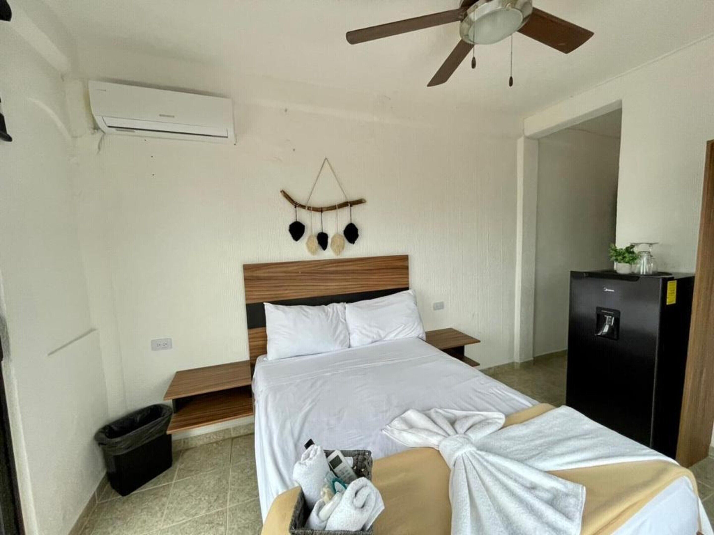 A hotel room with a bed, a ceiling fan, a small trash bin, and a minibar.
