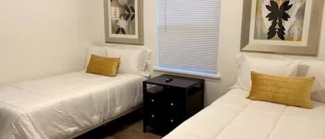Une chambre d’hôtel avec deux lits simples, une table de chevet, une fenêtre avec des stores et des œuvres d’art accrochées aux murs.