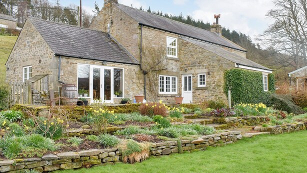 Una casa de piedra con jardín, con diversas plantas y flores.