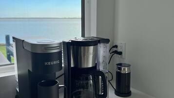 A Keurig coffee maker on a white countertop with a view of the sky and water outside.
