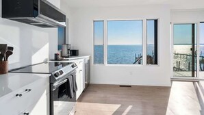 A modern kitchen with a view of the sea, large windows, and a sliding glass door to the outdoors. - Black Swan Beachfront Home with Jacuzzi year round (Hampton Bays)