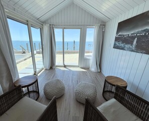Una habitación con vista a la playa, ventanas amplias, mobiliario de mimbre y un cartel en la pared.