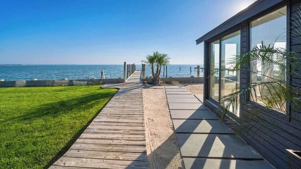 A modern building with large windows overlooking a beach. - Black Swan Beachfront Home with Jacuzzi year round (Hampton Bays)