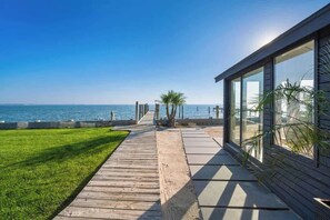 A modern building with large windows overlooking a beach. - Black Swan Beachfront Home with Jacuzzi year round (Hampton Bays)