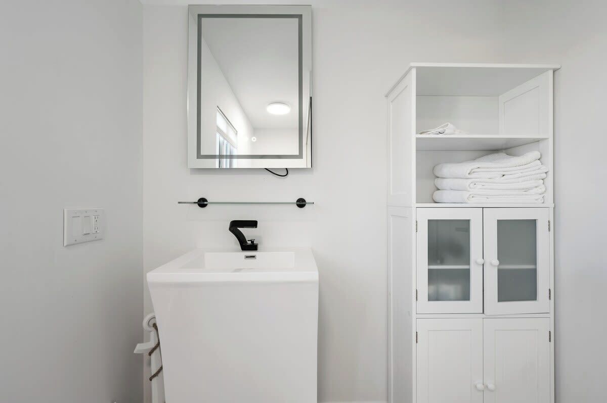 A white bathroom with a sink, mirror, and cabinet with towels.