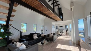 A spacious living area with a modern staircase, a dining area, and a kitchen. - Black Swan Beachfront Home with Jacuzzi year round (Hampton Bays)