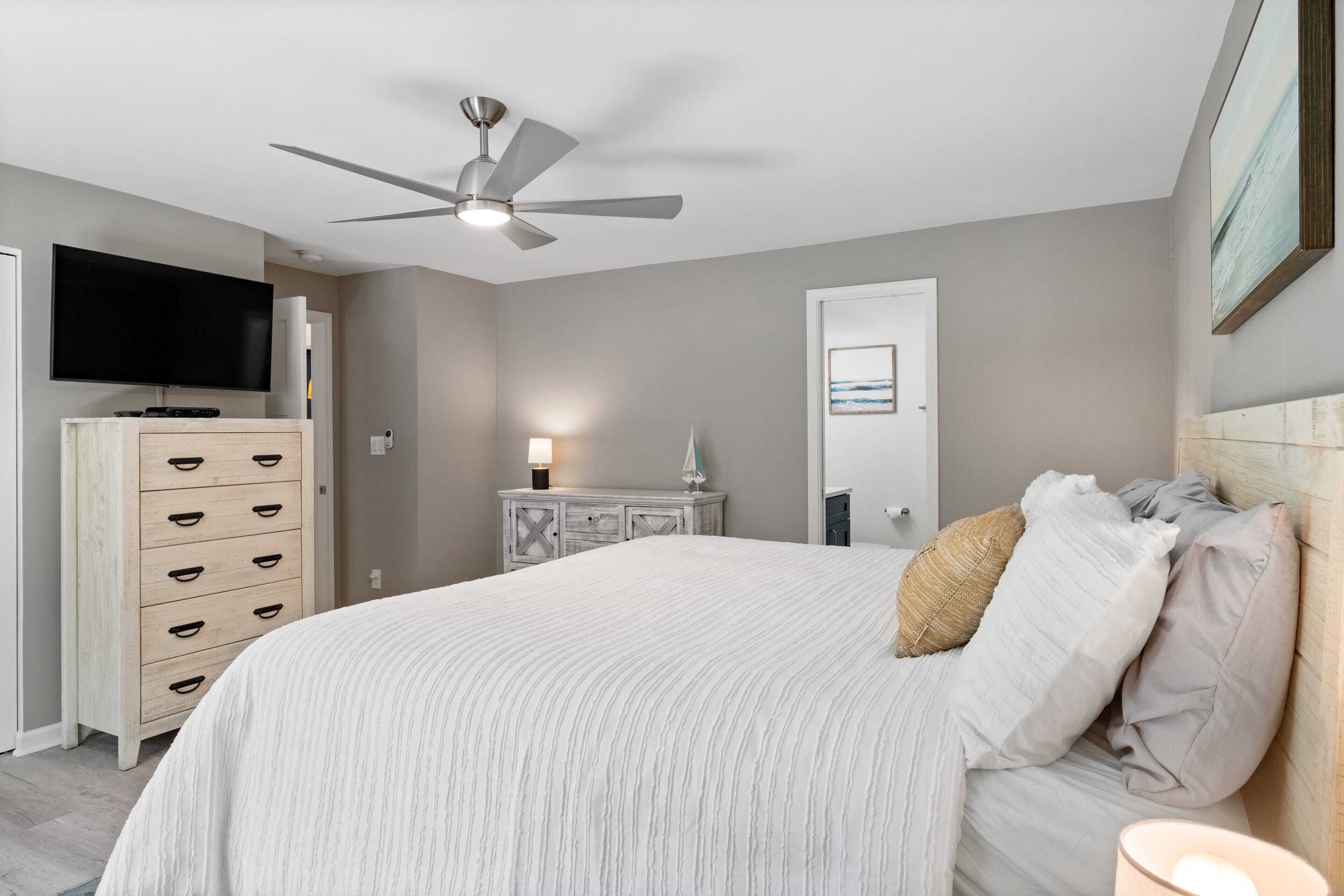 Une chambre à coucher avec un lit, un ventilateur de plafond, une commode, un téléviseur et une porte.