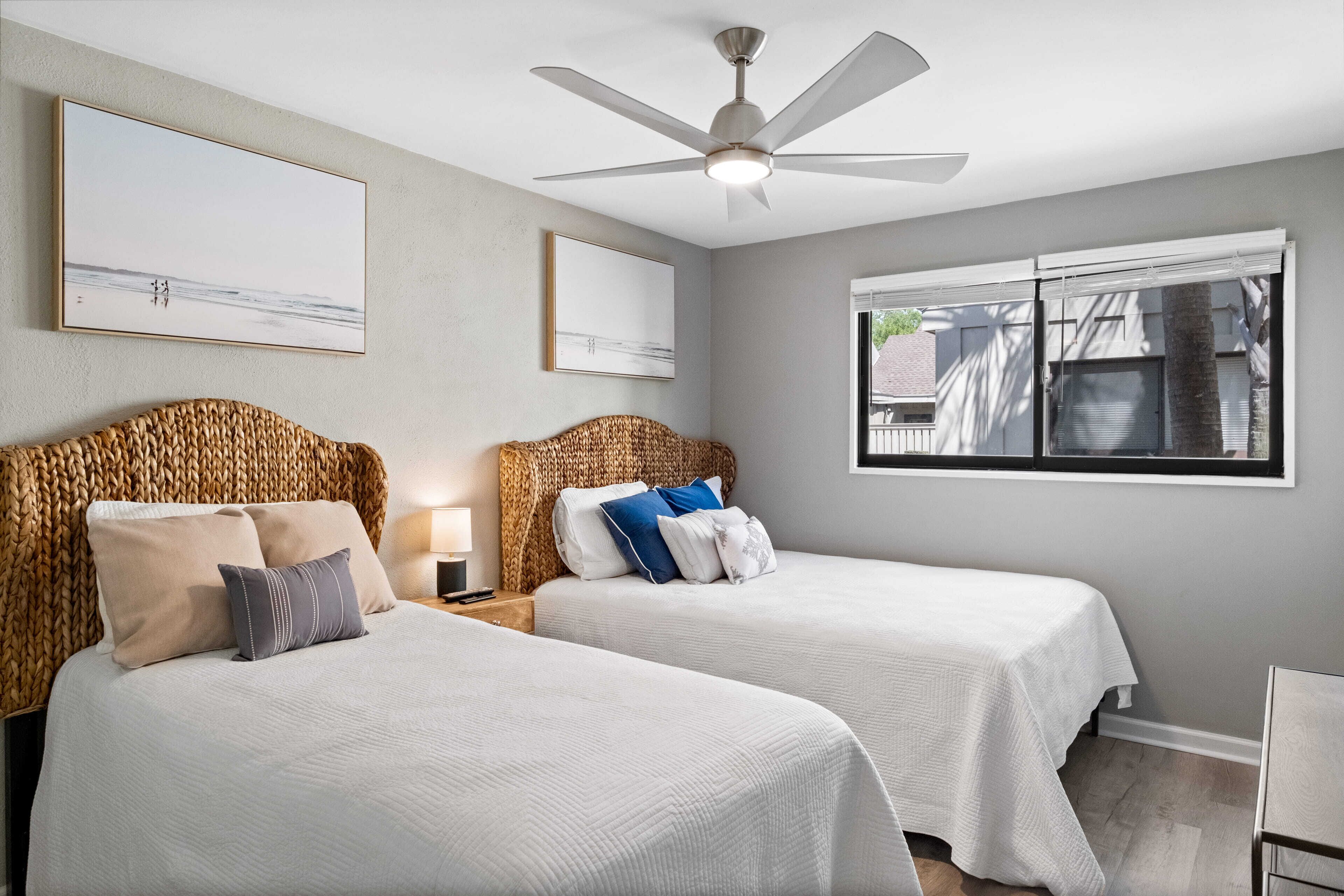Une chambre d’hôtel avec deux lits, un ventilateur de plafond et des œuvres d’art accrochées aux murs.