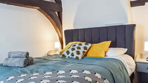 A bedroom with a dark headboard, a bed with a blue and white patterned bedspread, and two pillows, one yellow and one with a palm tree pattern. - 1 bedroom accommodation in Abingdon (Abingdon)