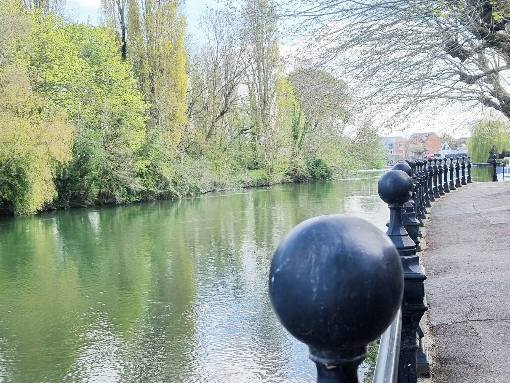 Une rivière paisible, bordée d’une rambarde en métal noir.