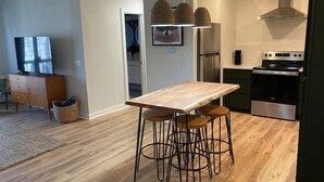 Eine moderne Küche mit Holztisch und Barhocker, Edelstahlgeräten und Pendelleuchten.