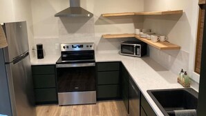 Eine kompakte Küche mit einem Edelstahlkühlschrank, einem eingebauten Backofen, einer Mikrowelle und einem Holzregal über der Spüle.
