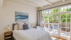Ein Schlafzimmer mit einem großen Bett, einem Nachttisch mit Lampe, einem Bild an der Wand und Blick ins Freie durch eine Schiebetür.