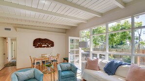 Ein geräumiges Wohnzimmer mit einem weißen Sofa, zwei blauen Sesseln, einem Esstisch mit Stühlen und einem großen Fenster mit Blick auf Grünflächen.