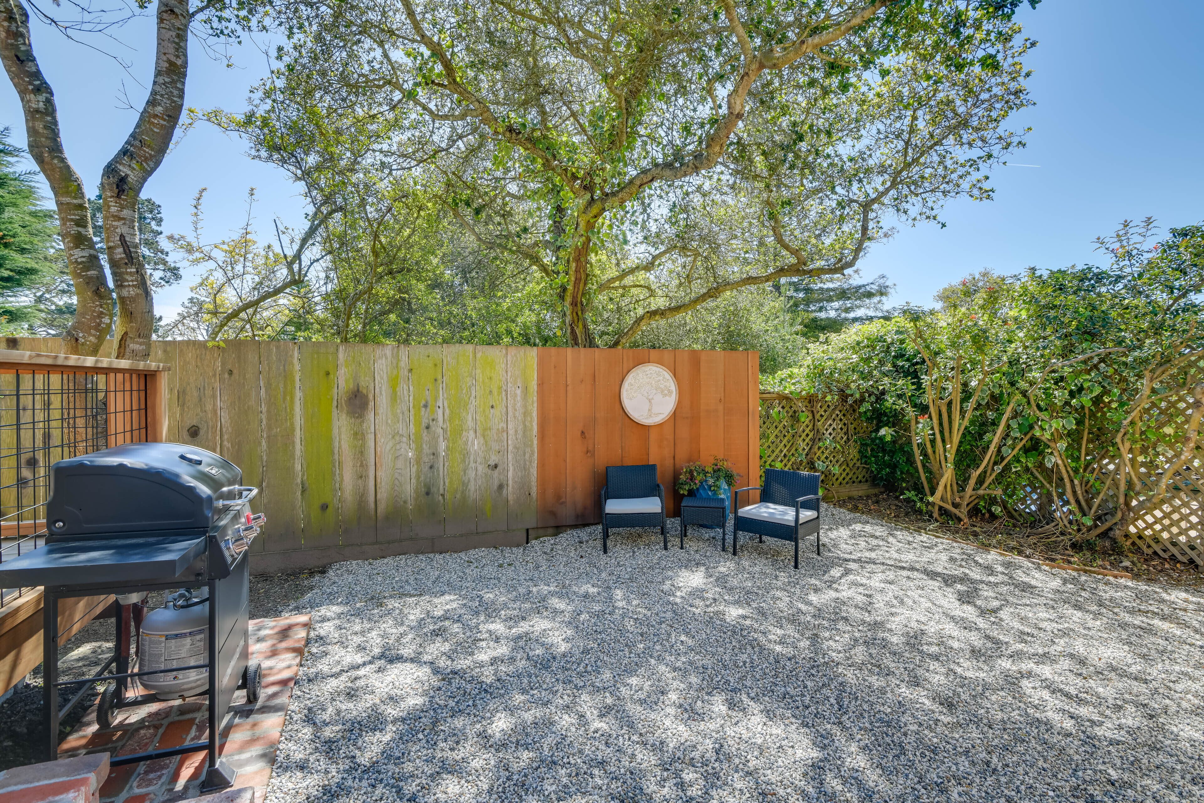 A backyard with a barbecue grill, two chairs, and a wooden wall with a circular design.