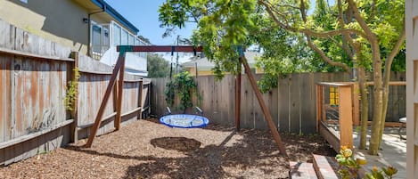 A backyard with a swing set, a trampoline, and a wooden fence.