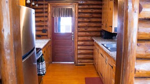 A log cabin kitchen with a wooden door, a refrigerator, a sink, and a window.