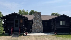 A log cabin with a stone chimney, a porch, and a small garden area.
