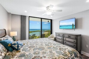 A bedroom with a large bed, a ceiling fan, a TV, and a balcony with a view of the ocean. - Sand Dollar Sunsets, a South Seas Oceanfront Condo (Marco Island)