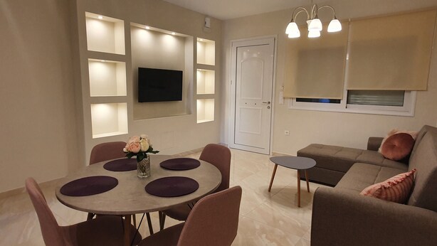 Una sala de estar moderna con comedor, que incluye una mesa redonda con sillas, un sofá y un televisor montado en la pared.