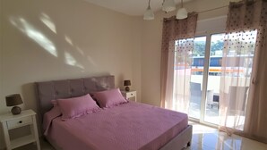 Un dormitorio con cama, mesitas de noche y ventana con cortinas.