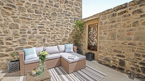 Un espace extérieur aménagé avec des murs en pierre, comprenant un canapé en osier, des coussins et un tapis à rayures.