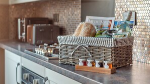 Un comptoir de cuisine sur lequel se trouve un panier en osier contenant du pain, une bouteille et un magazine.